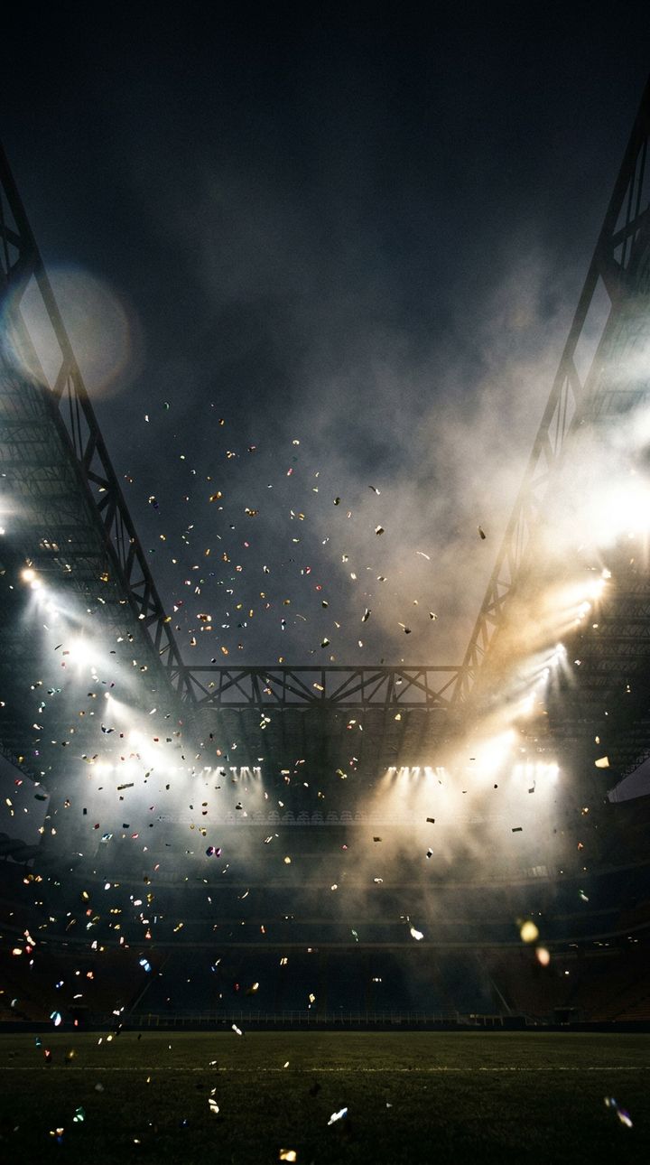 Stadium floodlights cutting through night haze with confetti in the air